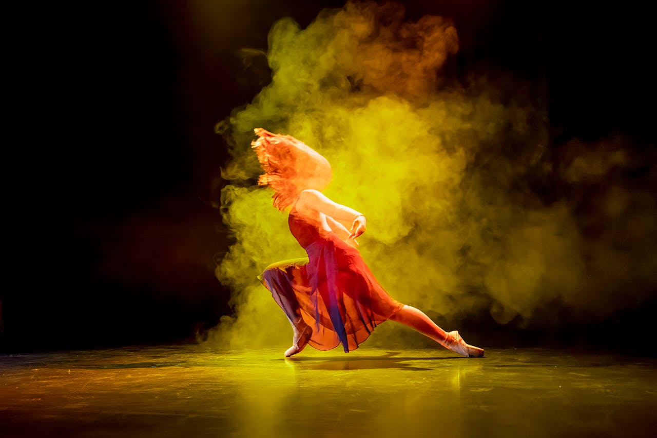 Dramatic shot of a ballet dancer poised with colorful smoke onstage.